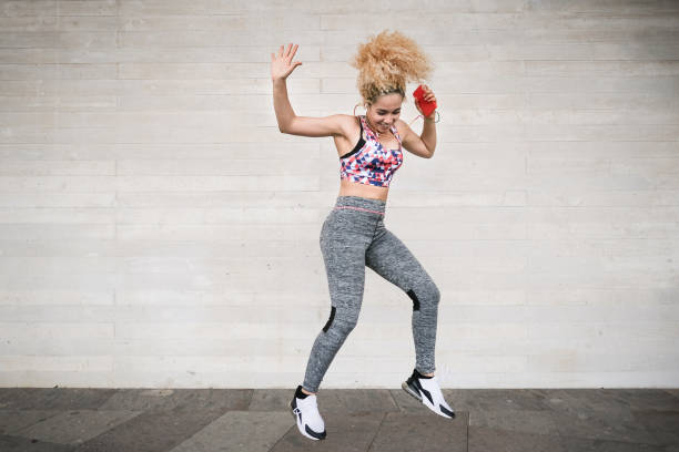 jeune femme dansant avec des écouteurs et la musique d’écoute de smartphone - femme multiraciale heureuse avec les cheveux bouclés blonds et sportswear - émotion, technologie et forme physique - fitness dance photos et images de collection