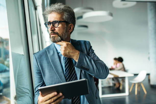 istock Happy senior businessman standing next to window 1255794602