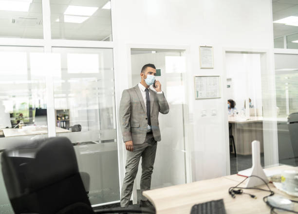 istock Safety in office: manager with face mask talking on phone in office 1255795545