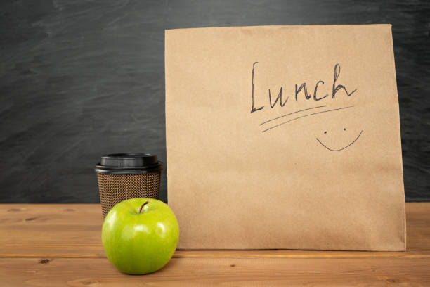 bolsa de almuerzo de papel marrón ecológico en la mesa de madera con manzana y taza de café. pizarra sobre fondo. volver al concepto de la escuela. - packed lunch lunch paper bag blackboard fotografías e imágenes de stock