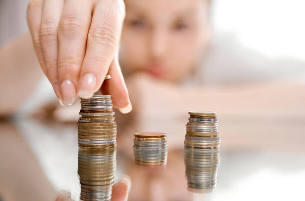 istock A blurnt woman in the background, a sharp hand in the foreground on a mirrored table collects stacks of coins 1255800888