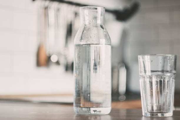 uma jarra de água na mesa de madeira da cozinha. garrafa de água. o conceito de um estilo de vida saudável - distilled water - fotografias e filmes do acervo