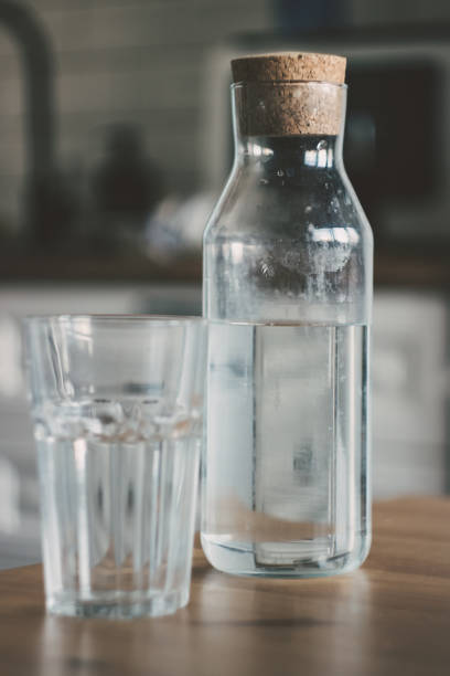 uma jarra de água na mesa de madeira da cozinha. garrafa de água. o conceito de um estilo de vida saudável - pouring water carafe glass - fotografias e filmes do acervo