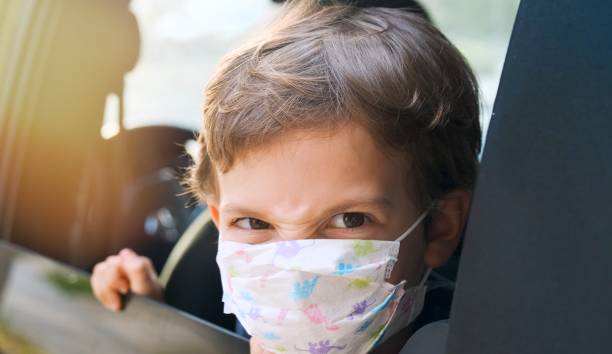 istock Angry little boy wearing a protective face mask looking at the camera through a car window 1255802774