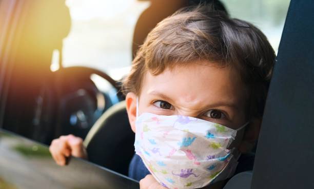 istock Angry little boy wearing a protective face mask looking at the camera through a car window 1255804528