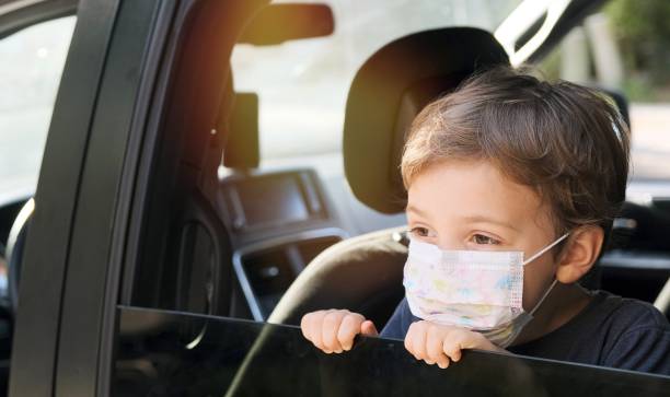 istock Little boy wearing a protective face mask looking away through a car window 1255812043