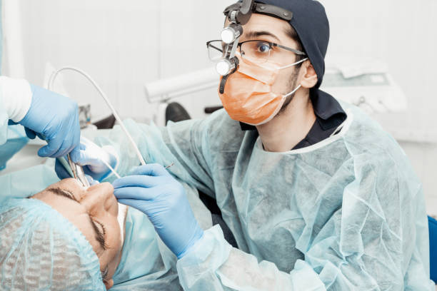 istock Patient and dentist during implant placement operation. Real operation. Tooth extraction, implants. Professional uniform and equipment of a dentist. Healthcare Equipping a doctorâs workplace. Dentistry 1255813486