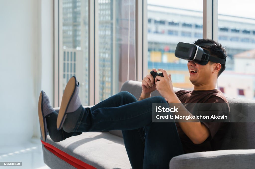 young asian man on bed holding game joystick and wear game 3d google glasses have fun playing video and console game at home Control Stock Photo