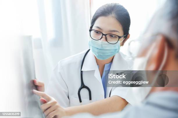 Asian Woman Doctor In Surgical Mask Giving Advice To Old Man Patient Stock Photo - Download Image Now