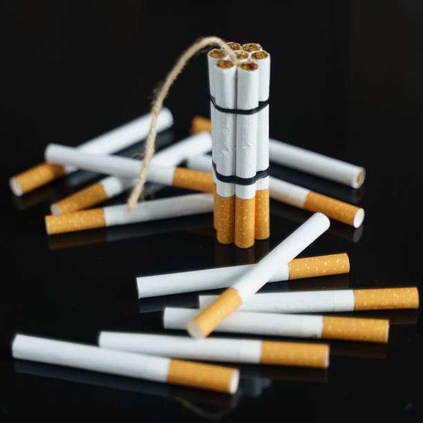istock Cigarettes, in the form of checkers with dynamite, stand among the scattered cigarettes on a black reflective surface. 1255843608