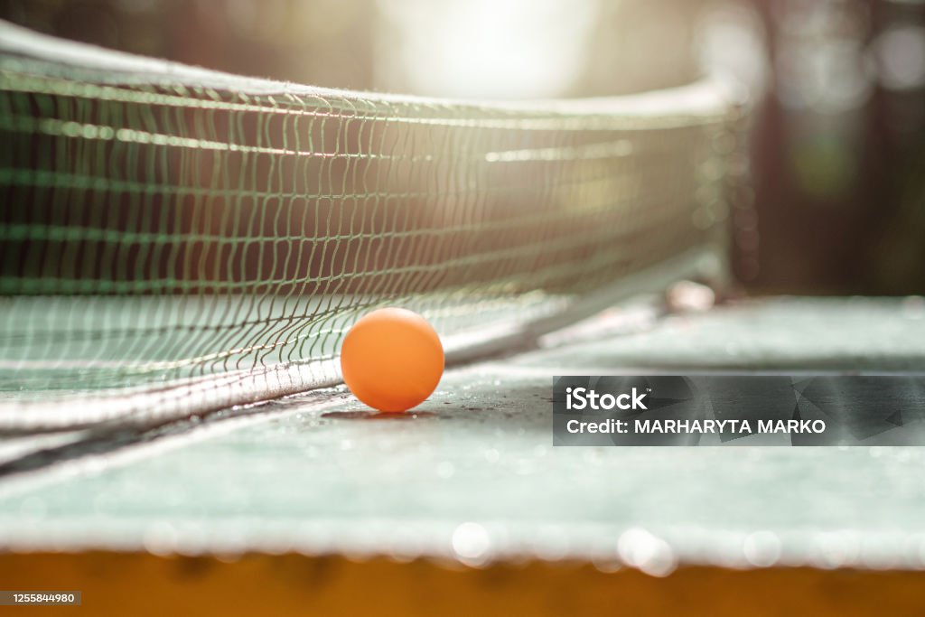 The concept of sports games, healthy lifestyle. Orange ball on a grid background on a ping pong table. Copy space, soft focus. The concept of sports games, healthy lifestyle. Orange ball on a grid background on a ping pong table. Copy space, soft focus Table Tennis Stock Photo