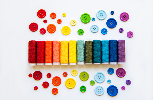 Spools of thread and buttons on the colors of the rainbow on a white background, flat lay