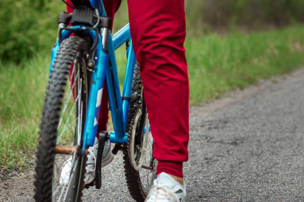 pernas nos pedais de uma bicicleta de perto, andando em uma estrada na floresta. o conceito de um estilo de vida saudável, treinamento cardio. copyspace. - pedal bicycle sports training cycling - fotografias e filmes do acervo