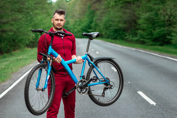istock Athletic Man in a tracksuit holds a bicycle on his shoulders while standing on the road in the forest. The concept of a healthy lifestyle, cardio training. Copyspace. 1255848319