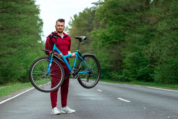 istock Athletic Man in a tracksuit holds a bicycle on his shoulders while standing on the road in the forest. The concept of a healthy lifestyle, cardio training. Copyspace. 1255848326