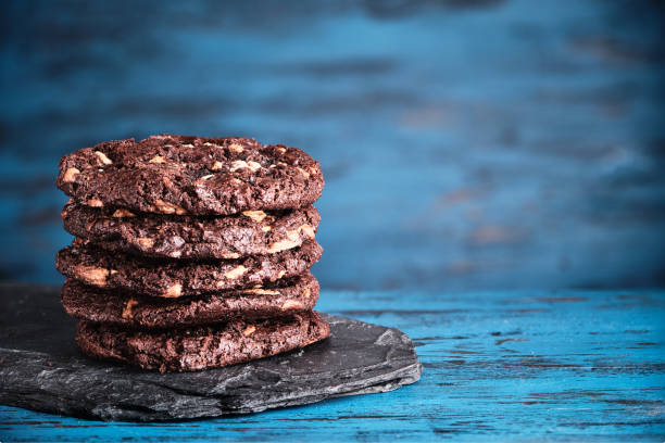 stapel von chokolate kekse mit kakao, schokolade und haselnüsse auf blauem holzhintergrund. - quarterback sack stock-fotos und bilder