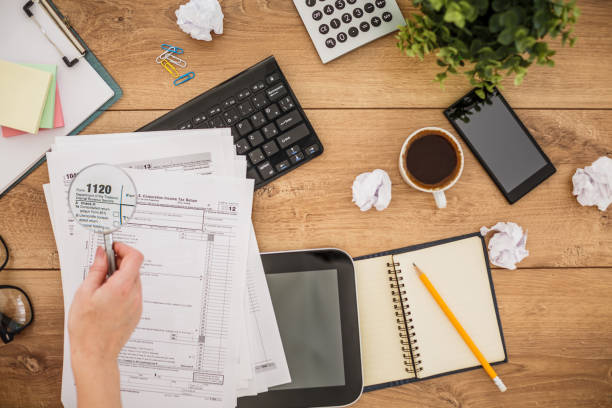 istock Female hand holding a magnifying glass over some paperwork on an office desk 1255850683