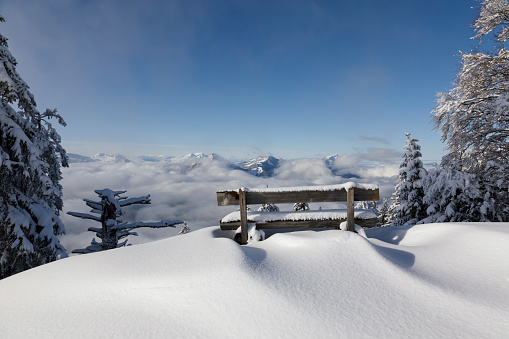 Snow-covered bench on Rotenflue in the canton of Schwyz with a view of the sea of fog in the valley in central Switzerland