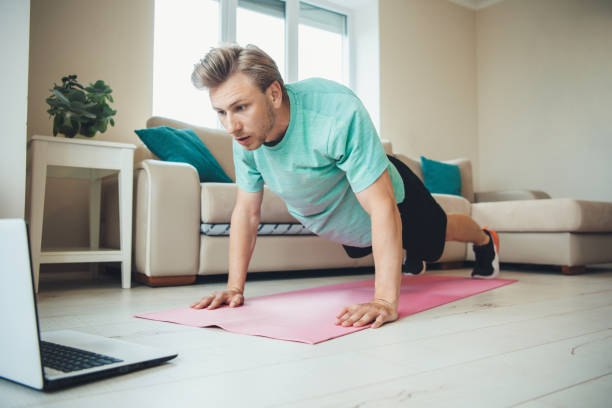 istock Blonde caucasian man with bristle doing push-ups on the floor using a laptop 1255851202