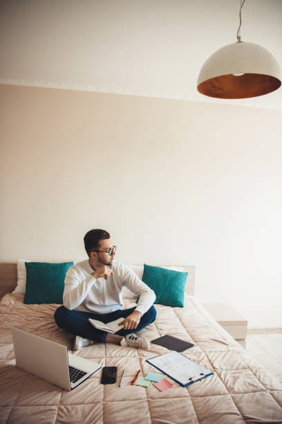 istock Thinking caucasian man with beard and eyeglasses is working in bed with a computer and documents 1255851779