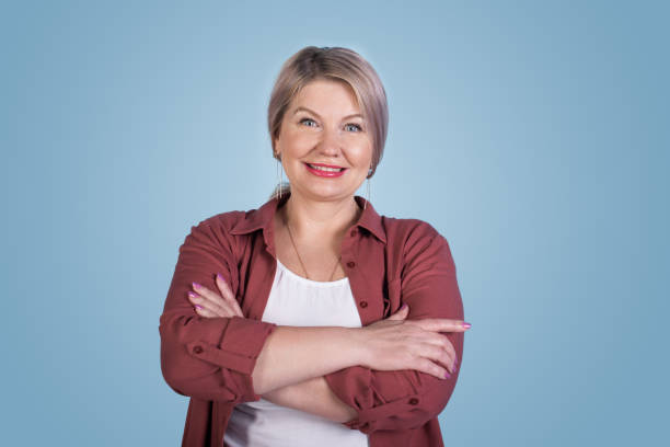 istock Charming senior woman with crossed hands smiling at camera on a blue studio wall 1255854140