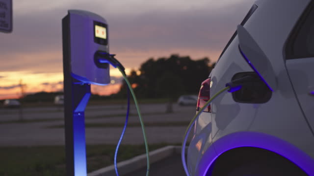 Slow motion shot of a vehicle being charged at blue energy charging station at dusk. Shoot in 8K resolution.