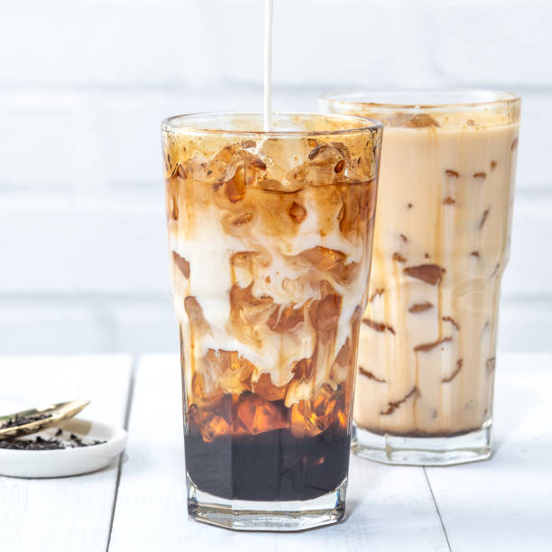 istock Making bubble tea, pouring blend milk tea into brown sugar pattern drinking glass cup on white wooden table background. 1255857140
