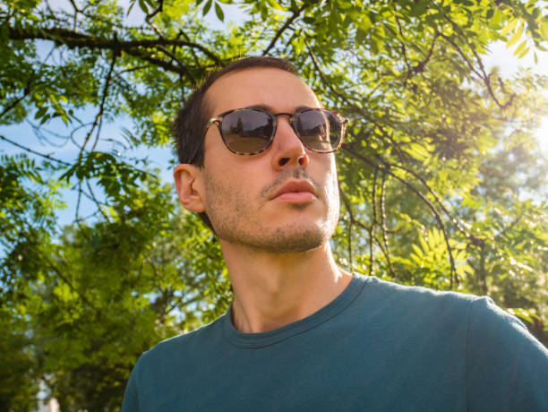 portret młodego mężczyzny nosi okulary przeciwsłoneczne. zielone drzewa lasu na tle. promienie słoneczne biją na okulary, spolaryzowanej koncepcji obiektywu. - polarization zdjęcia i obrazy z banku zdjęć