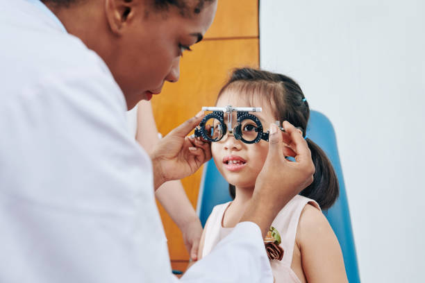Girl visiting pediatric optometrist Pediatric optometrist helping little girl to put on test glasses when checking her eyesight myopia photos stock pictures, royalty-free photos & images