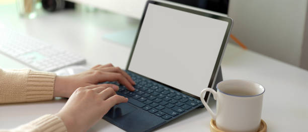istock Female entrepreneur hands typing on mock-up tablet keyboard with coffee cup and computer device on table 1255860354