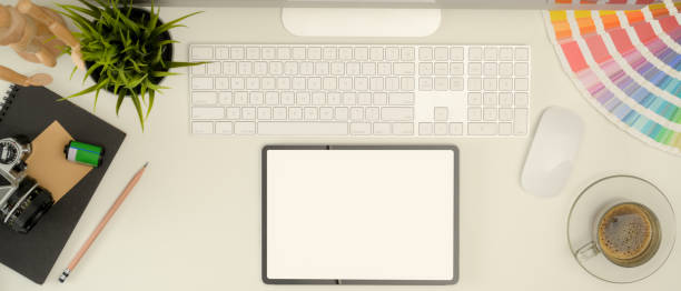 istock Mock up digital tablet on office desk with computer device, colour swatch, stationery, camera and coffee cup 1255861442