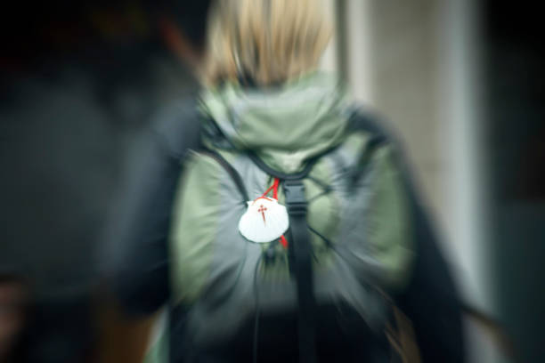 Rear view of defocused pilgrim in the 'camino de santiago', backpack and scallop shell symbol with traditional cross. Santiago de Compostela, Galicia, Spain.