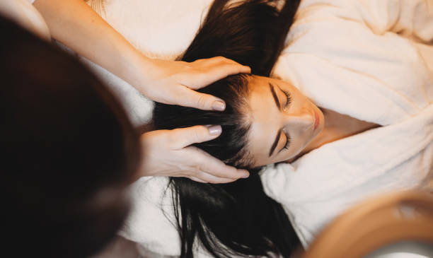 mujer caucásica con el pelo largo y negro acostado y tener un procedimiento de masaje de la cabeza del spa - head massage massaging facial massage beautician fotografías e imágenes de stock