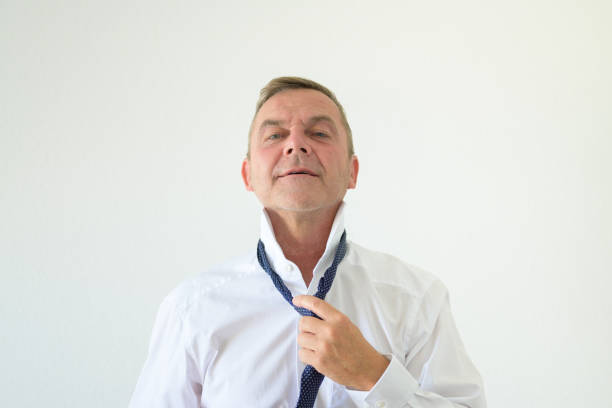 Middle-aged man loosens his necktie with his hand in a frontal portrait over a white background