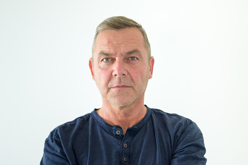 Enigmatic solemn man staring at the camera with a deadpan serious expression in a head and shoulders portrait on a white background