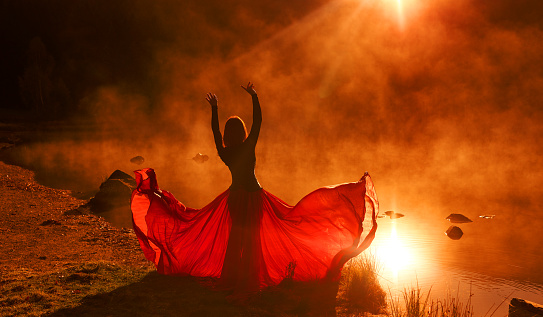 Rear view of woman with red skirt posing at sunset looking at view with arms outstretched feeling free