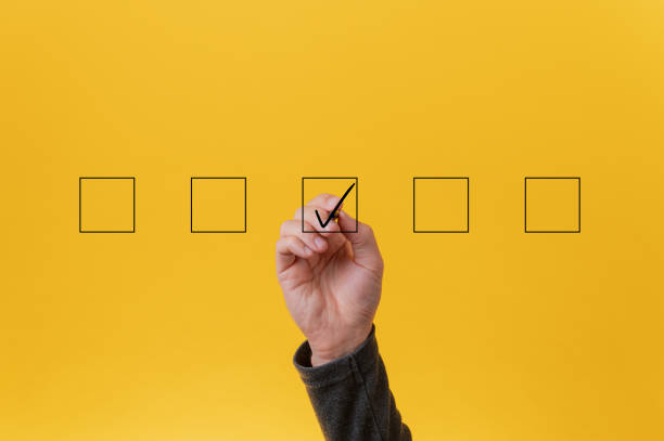 Drawing a check mark in the middle box in a row of five Male hand drawing a check mark in the middle box in a row of five. Over yellow background. checkbox photos stock pictures, royalty-free photos & images