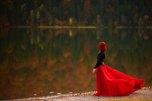 Profile view of redhead queen wearing red dress at the lake looking at view