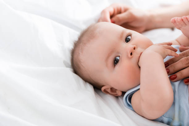 istock mother touching cute baby boy looking at camera while sucking hand 1255871905