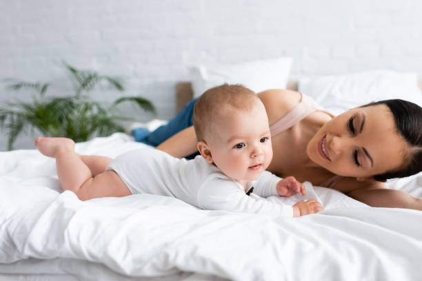 istock happy mother looking at barefoot infant son on bed 1255871907