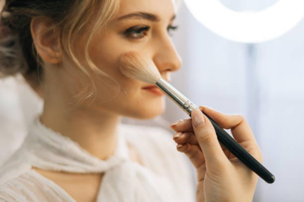 close-up of make-up artist putting rouge on cheek of young woman using brush - make up cosmetics women make up brush imagens e fotografias de stock