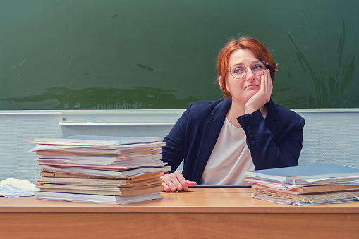 Portrait of a sad teacher at the school desk at the blackboard