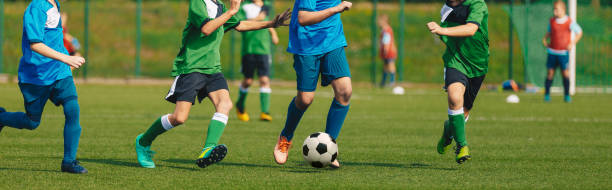 Horizontal Image of Soccer Competition. Junior Level Football Match. Players Running and Kicking Classic Soccer Ball. Goalkeeper in the Background. Two Teams Compete in School Tournament Horizontal Image of Soccer Competition. Junior Level Football Match. Players Running and Kicking Classic Soccer Ball. Goalkeeper in the Background. Two Teams Compete in School Tournament club soccer photos stock pictures, royalty-free photos & images