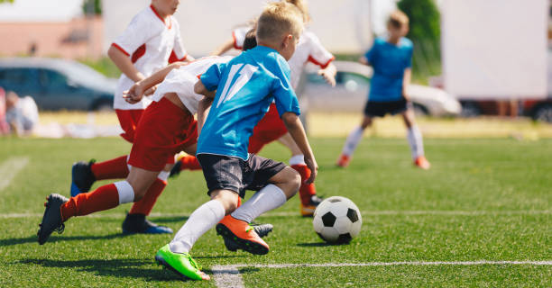 サッカーボールアクションで走っているサッカー選手。学校のスポーツ競技の子供たち。子供サッカー大会の水平サッカーイメージ - 子供サッカー ストックフォトと画像