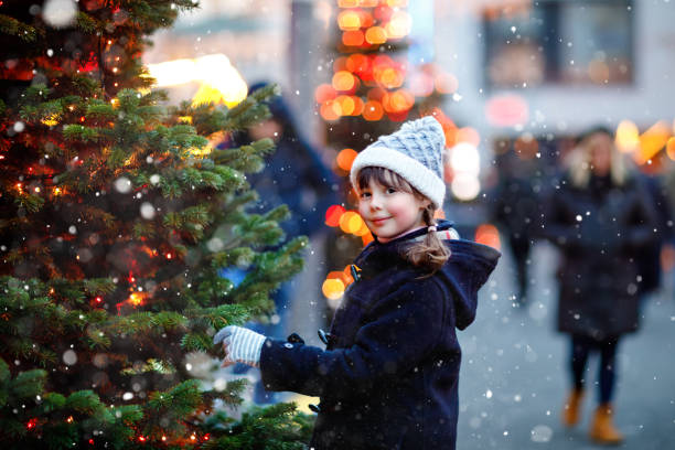 menina criança bonita se divertindo no mercado tradicional de natal durante a forte queda de neve. criança feliz desfrutando do tradicional mercado familiar na alemanha. estudante de pé perto de árvore de natal iluminada. - hot chocolate hot drink heat drinking - fotografias e filmes do acervo