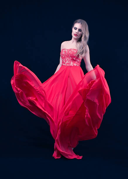 istock Young Blonde With a Red Silky Dress, That is Flying,  Looking Down, on Deep Blue Background. Fashion Position 1255885693