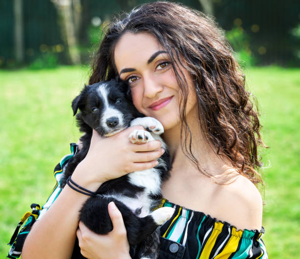 Female brunette model holding adorable border collie puppy up to her cheek stock photo