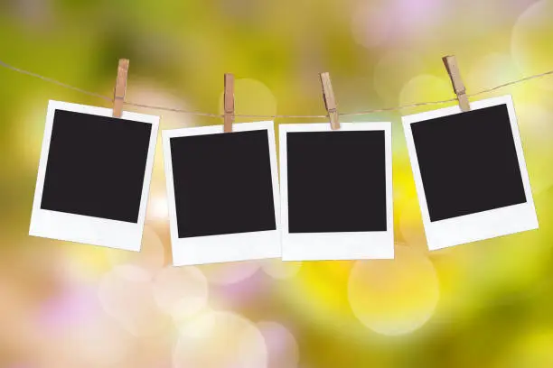 Photo of Four blank instant photo frames hanging on a rope, on green blur nature background