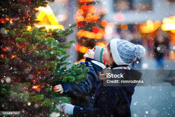 Two Little Kids Boy And Girl Having Fun On Traditional Christmas Market During Strong Snowfall Happy Children Enjoying Traditional Family Market In Germany Twins Standing By Illuminated Xmas Tree Stock Photo - Download Image Now