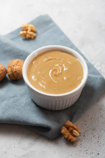 Walnut butter on the gray concrete background. It is rich in several nutrients, including protein and magnesium, which may help protect the heart and manage blood sugar and body weight. Top view